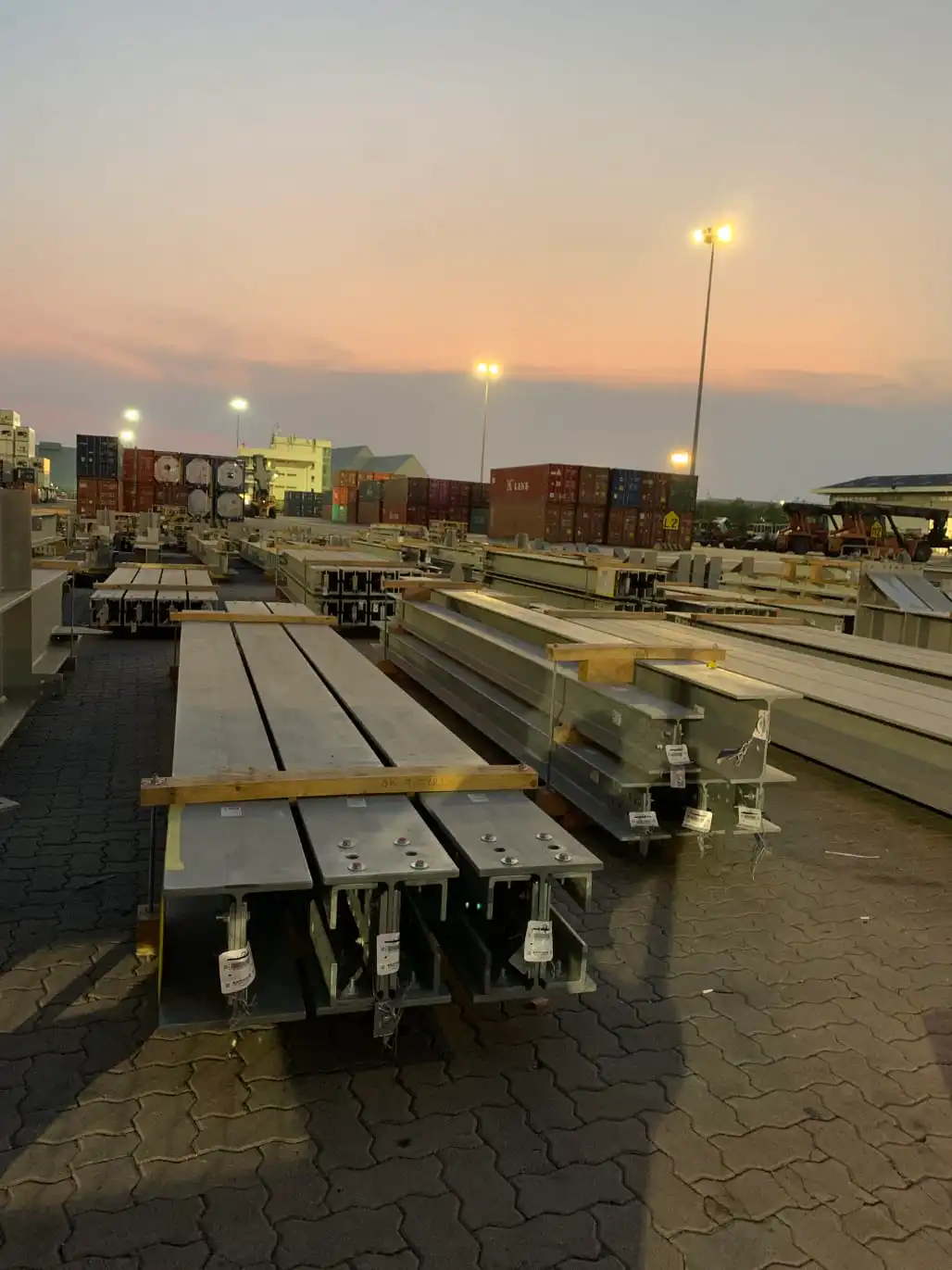 เหล็กโครงประกอบเรียงในลานส่งของ | Steel beams stacked in shipping yard